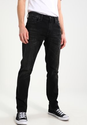 Zwarte denim jeans met een tapered fit, voorzien van subtiele vervaging en een vijfzaksontwerp. gedragen met zwarte canvas sneakers.