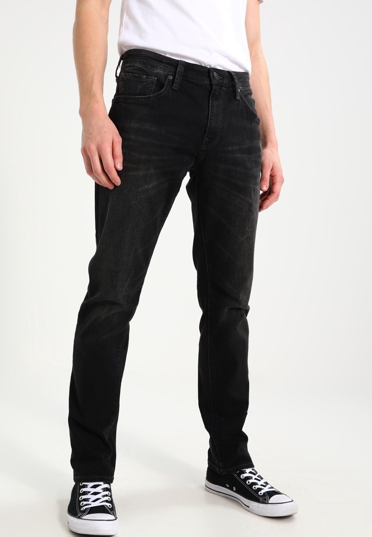 Vaqueros de denim negro con un corte ajustado, que presentan un ligero desgaste y un diseño de cinco bolsillos. Se llevan con zapatillas de lona negras.
