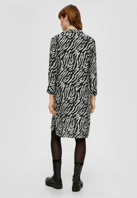 Langärmliges Kleid im schwarz-weißen Wellenmuster; aus weichem Stoff; knielang mit seitlichen Schlitzen; kombiniert mit schwarzen Ankle Boots.