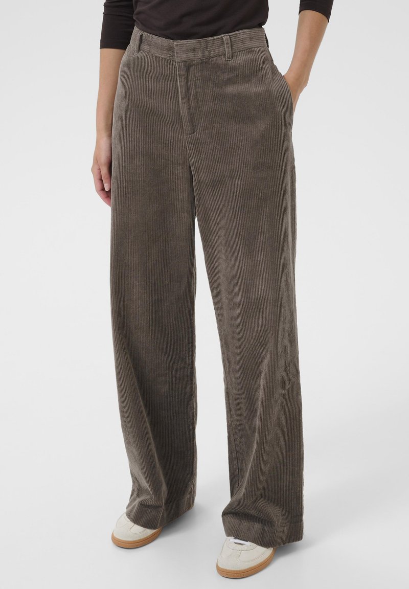 Bruine corduroy wijde broek met verticale strepen, voorzien van een hoge tailleband en zijzakken, gecombineerd met lichtgekleurde sneakers.