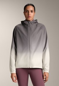 Ľahká bunda s kapucňou v gradientnom dizajne, prechádzajúca od tmavosivej po bielu. Vybavená elastickými manžetami a plným predným zipsom.