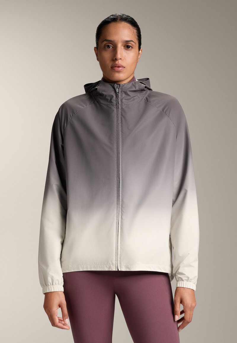 Ľahká bunda s kapucňou v gradientnom dizajne, prechádzajúca od tmavosivej po bielu. Vybavená elastickými manžetami a plným predným zipsom.