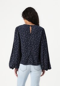 Blusa floreale blu mare con maniche corte arricciate, dettagli di plissettatura sul retro e apertura a chiave sul colletto. Tessuto morbido e leggero.