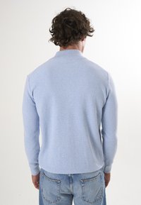 Pull en tricot côtelé bleu clair avec col et manches longues, associé à un jean en denim clair, vu de dos.