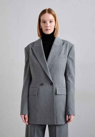Grå oversized blazer med to knapper, slagkraver og frontlommer. Båret over en sort turtleneck med struktureret stof.