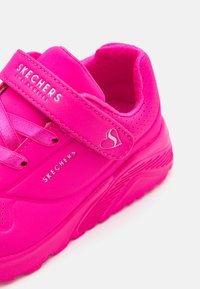 Ružová sneakerka Skechers s hladkým syntetickým vrchom, suchým zipsom a perforovanými detailmi. Má vystlanú podrážku a logo.