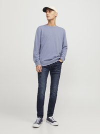 Vaaleanlila huppari, tummansiniset farkut, joissa on hienoa kulutusta, valkoiset lenkkarit ja beige baseball-hattu, jossa on musta lippa.