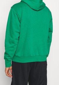 Sweatshirt à capuche verte en tissu doux. Présente une coupe décontractée, des poignets côtelés et une poche kangourou à l'avant.