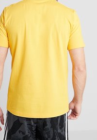 Camiseta de algodón amarilla con mangas cortas y un cuello redondo, presenta una textura suave y un diseño simple y sin adornos.