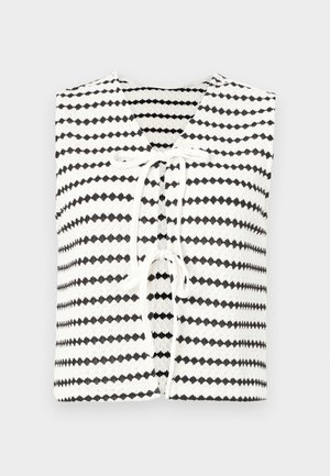 Valge lühikeste varrukatega tipp, millel on korduv musta kihi muster, kaelas sidumisega ja struktureeritud kudumiskangast.