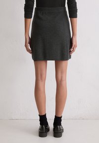 Grijze wollen rok met een aansluitende tailleband, die iets uitloopt bij de zoom. Gdragend met zwarte geribbelde sokken en loafers. Glad textuur en eenvoudig ontwerp.