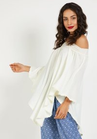 Top blanco sin mangas con volantes en las mangas y cuello texturizado, combinado con pantalones azules estampados que presentan formas de rombos.