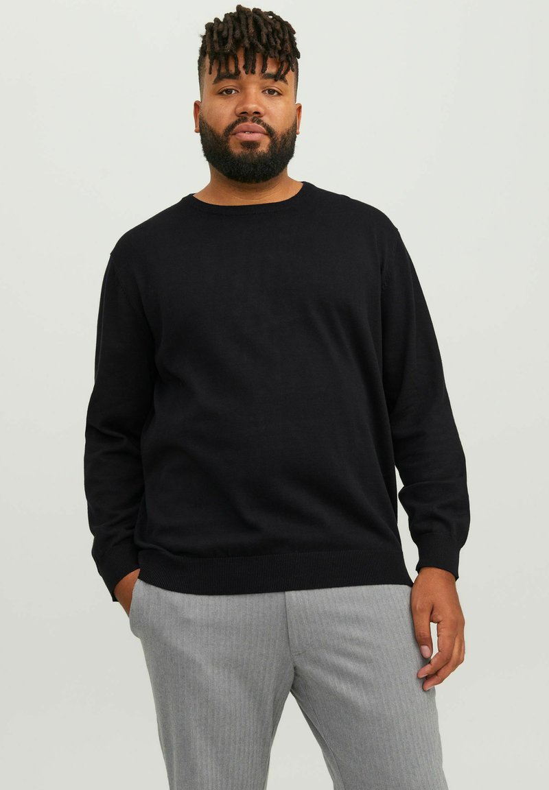 Pulover negru tricotat, cu guler rotund, mâneci lungi și manșete cu zimți. Asortat cu pantaloni gri cu dungi. Textură netedă, design casual.