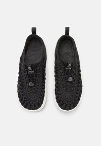 Svarta sportskor med vävd ovandel, texturerad design och snörlöst stängningssystem. Har en vit gummisål och dragögon för enkel påtagning.