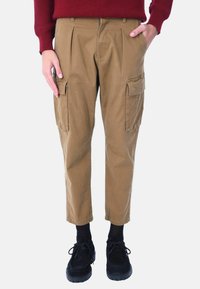 Pantaloni cargo color khaki, con tasche laterali, pieghe, una vestibilità rilassata e gambe affusolate, abbinati a scarpe nere e calzini scuri.