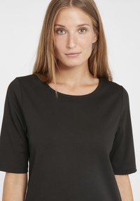 Top nero a maniche corte con scollatura rotonda. Realizzato in tessuto morbido con uno stile aderente, presenta dettagli di cucitura sottili.