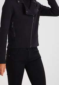 Černá zkrácená bunda z jemného materiálu v motorkářském stylu. Obsahuje asymetrický zip, dvě přední kapsy a hladký povrch.
