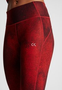 Czerwone legginsy z wysokim stanem, z teksturowanym gradientowym wzorem, z kontrastowym białym logo. Gładki materiał z przeszytymi akcentami.