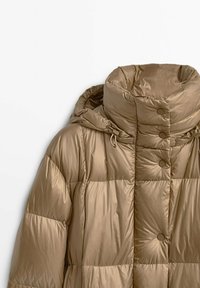 Giacca a vento color marrone chiaro, con colletto alto, dettagli in bottoni e design trapuntato. Realizzata in un materiale lucido e resistente all'acqua.
