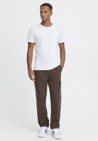 White short-sleeve t-shirt paired with brown cargo pants featuring side pockets, worn with white sneakers. Simple and functional design.