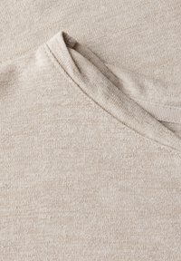 Béžová pletenina s jemnou texturou, s volným výstřihem a jemnými barevnými variacemi. Ukazuje detailní šití a zpracování.