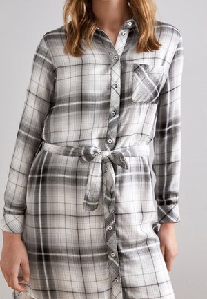 Schwarz-weiß kariertes Kleid mit langen Ärmeln, Knopfverschluss, Brusttasche und einem gebundenen Taillendetail, aus weichem Stoff mit glatter Textur gefertigt.