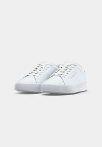 Pari sneakers putih model low-top dengan tali sepatu, bermerek "Tommy Hilfiger" di sisi dan lidah sepatu, diletakkan di atas latar belakang putih polos.