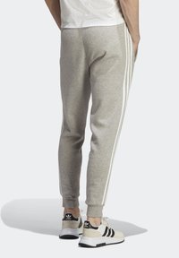 Pantalones de chándal grises con rayas blancas en los lados, de corte ajustado, fabricados con un tejido suave. Combinados con zapatillas ligeras que presentan acentos en negro y blanco.
