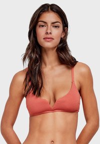 Finitura liscia, reggiseno di colore pesca con trama, design a profonda scollatura a V e spalline regolabili, presentato su uno sfondo neutro.