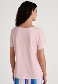 Roze katoenen t-shirt met korte mouwen en kantafwerking aan de zoom. Rond de halslijn en een comfortabele pasvorm. Gecombineerd met gestreepte pyjamabroek.