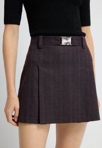 Violet nederdel med lodrette striber, plisseret design og en sølv rektangulær spænde. Lavet af et struktureret stof.