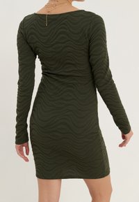 Robe à manches longues de couleur vert olive, présentant un motif ondulé texturé, une silhouette ajustée et un col rond. Le matériau semble extensible et lisse.
