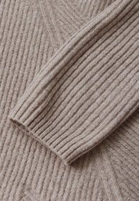 Beige Strickpullover mit gerippter Textur und diagonalen Mustern. Verfügt über einen umgeschlagenen Ärmel, der das weiche Wollmaterial zur Schau stellt.