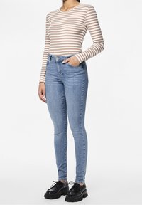 Randig långärmad topp i beige och vitt, kombinerad med ljusblå skinny jeans; svarta skor med kraftig sula; händer i fickorna, minimal detalj.