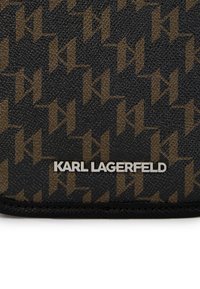 Melnas teksturētas materiāls ar atk�ārtojošu brūna logotipa rakstu. Sudraba "KARL LAGERFELD" zīmols atrodas apakšā.