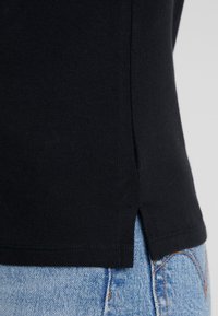 Svart bomulls-t-shirt med en texturerad yta, med en sidöppning och kontrasterande blå denim nedanför. Rent sytt vid fållen.