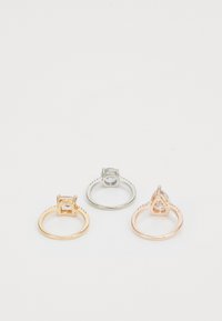 Tres anillos: un anillo de oro con una piedra rectangular, un anillo de plata con una piedra redonda y un anillo de oro rosa con una piedra en forma de lágrima.