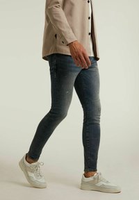 Jean bleu ajusté avec des zones décolorées, un léger effet usé et une texture lisse. Associé à des baskets blanches avec des accents texturés.