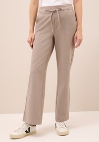Beige wijde broek met verstelbare koord in de taille, gedragen met witte sneakers met een zwart V-logo.