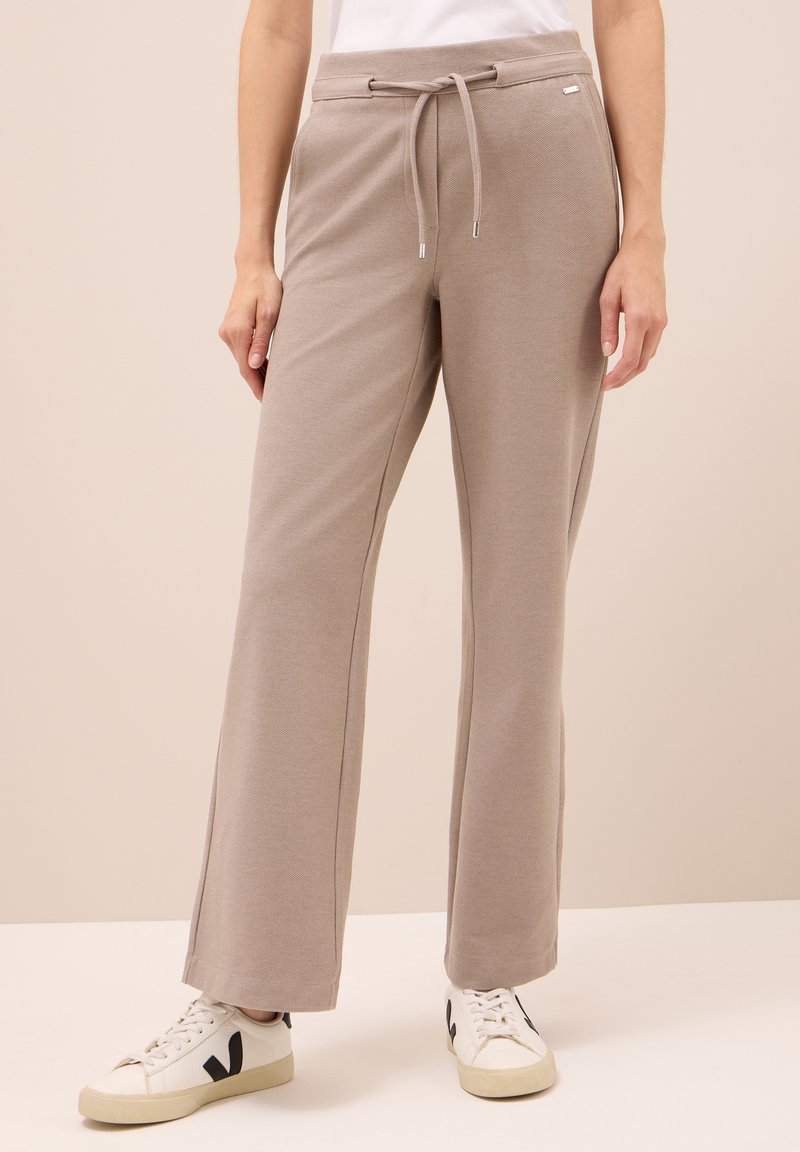 Beige wijde broek met verstelbare koord in de taille, gedragen met witte sneakers met een zwart V-logo.