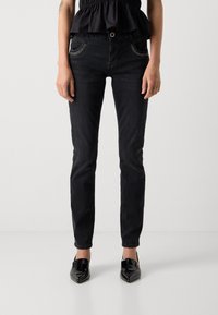 Crne skinny traperice izrađene od denima, sa slim fit krojem, ukrasno prošivene džepove i klasično dugme za zatvaranje u struku.