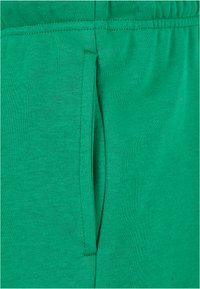 Grønt bomullsstoff med glatt tekstur, med en sidelomme og elastisk midje. Stoffet er elastisk og tett vevd.