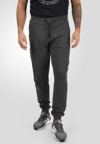Mørkegrå joggebukser med snor i midjen, sidelommer, ribbede mansjetter og smal passform, kombinert med grå joggesko.