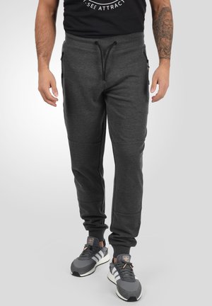 Dark gray sweatpants with a drawstring waist, side pockets, ribbed cuffs, and a slim fit, paired with gray athletic shoes.