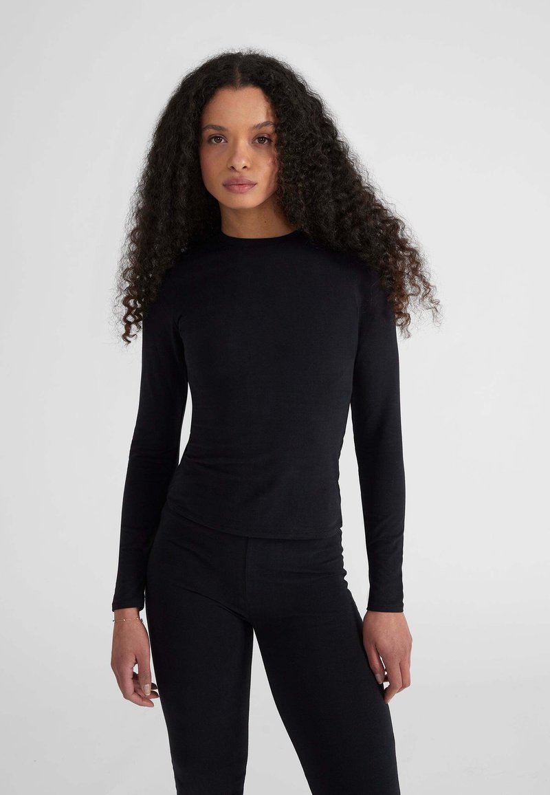 Top nero a maniche lunghe realizzato in tessuto elastico, con scollatura rotonda e silhouette aderente, abbinato a leggings coordinati.