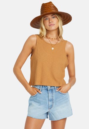 Brown ribbed tank top with a relaxed fit, paired with light blue denim shorts. The model wears a wide-brimmed straw hat and layered necklaces.