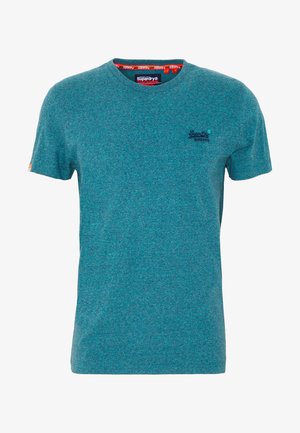 Camiseta de manga corta en color teal, fabricada en una suave tela texturizada, con cuello redondo y un logotipo en el lado izquierdo del pecho. La etiqueta muestra el nombre de la marca en el interior del cuello.