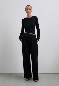 Zwart, gebreid langslangrijk shirt met een getailleerde pasvorm, gecombineerd met zwart, hoogwaterbroek met brede pijpen. Zilveren gesp met studs als accent.