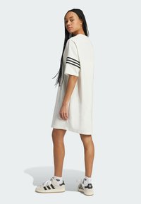 Abito bianco oversize con maniche corte e strisce nere sulle spalle. Abbinato a sneaker bianco e nere, trecce texturizzate visibili.