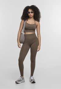 Top corto atletico marrone e leggings a vita alta in tessuto elastico. Gli accessori includono una borsa a spalla grigia trapuntata e sneakers grigie.